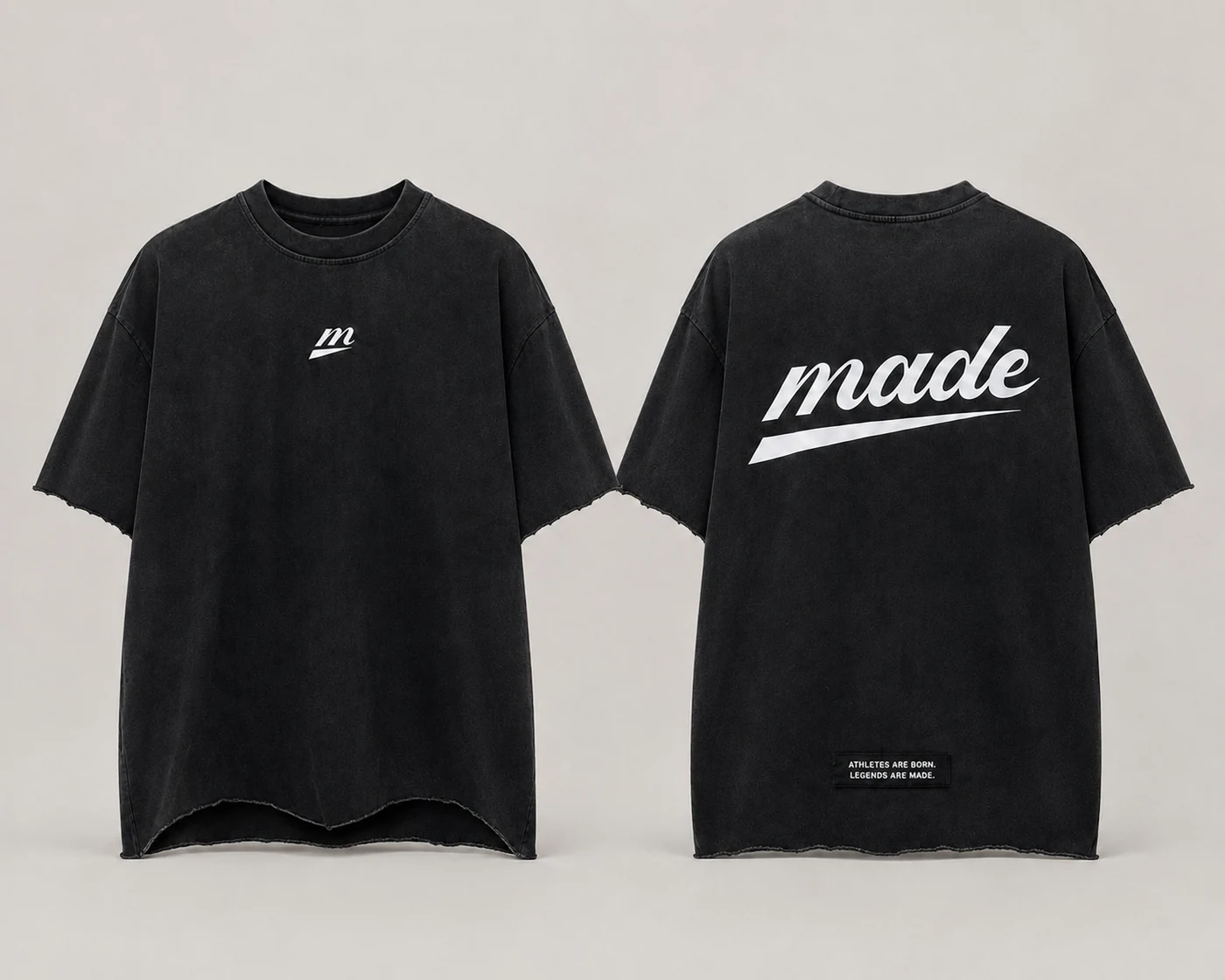 MADE Signature Tee in washed black, shown front and back — white m icon centred at chest, large white made wordmark with the glide underline across the back, and a black woven patch reading “Athletes are born. Legends are made.” above the raw curved hem